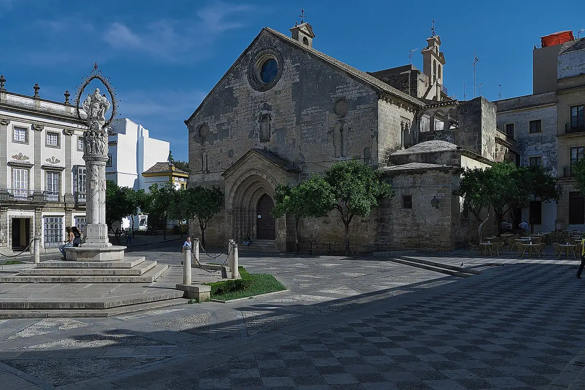 A paved square in the old town of Jerez with a stone Gothic church and a tall column in front of a palace facade