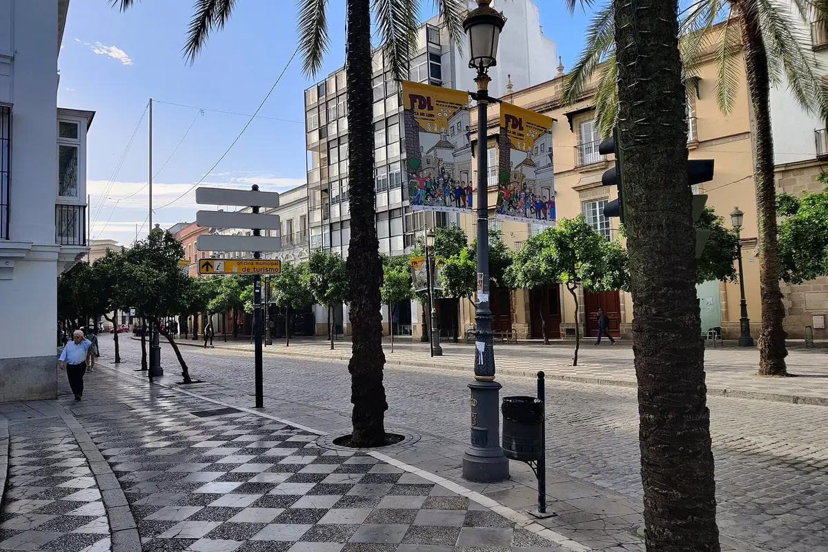 A paved pedestrian street in central Jerez lined with palms and orange trees, with banners hanging from the lamp posts