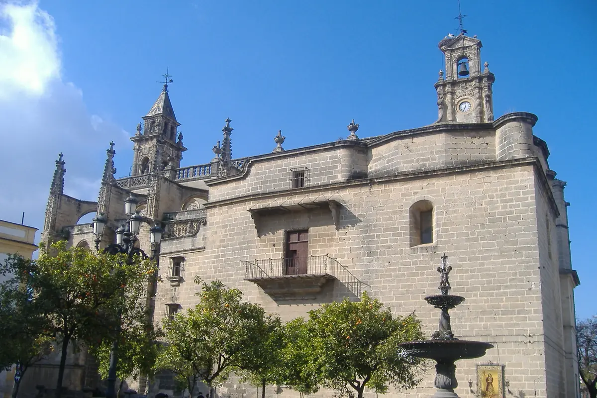 The stone side wall and bell tower of the church of Santiago in Jerez, with orange trees and a small fountain in front